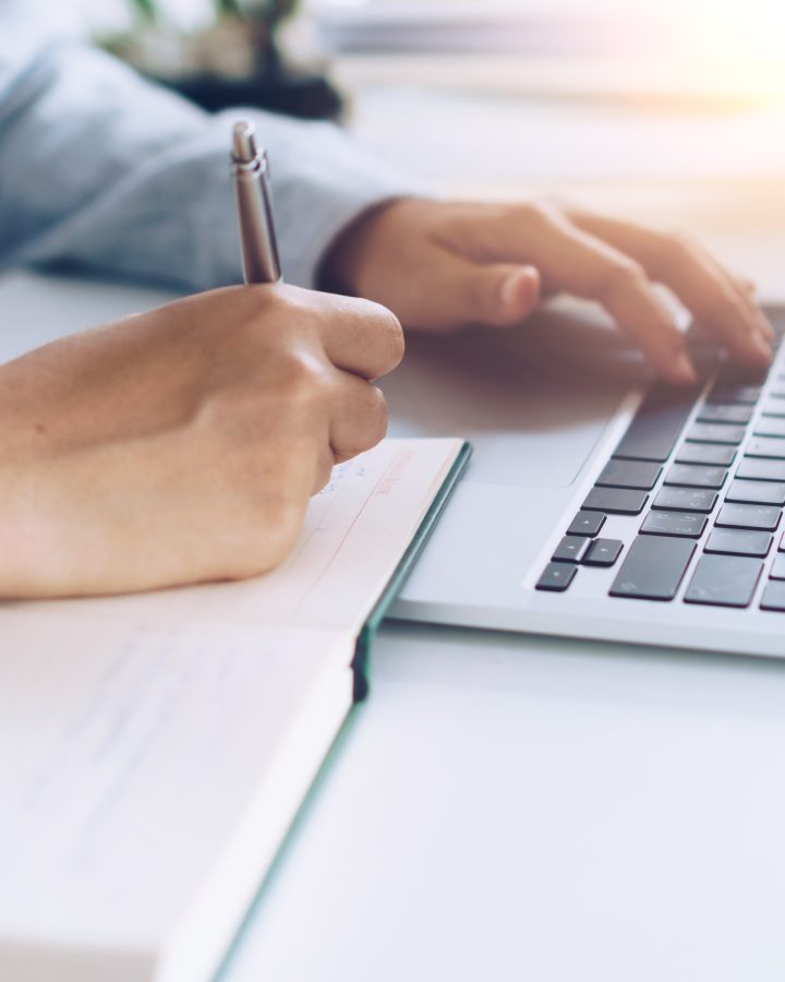 Woman is writing in planner notebook while using laptop to work or plan with workspace at home. Education business lifestyle concept.